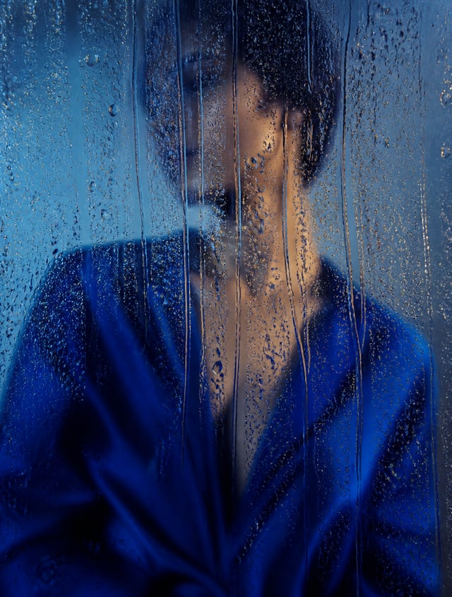 A cinematic editorial fashion photograph of a figure in a saturated cobalt-blue silk garment standin