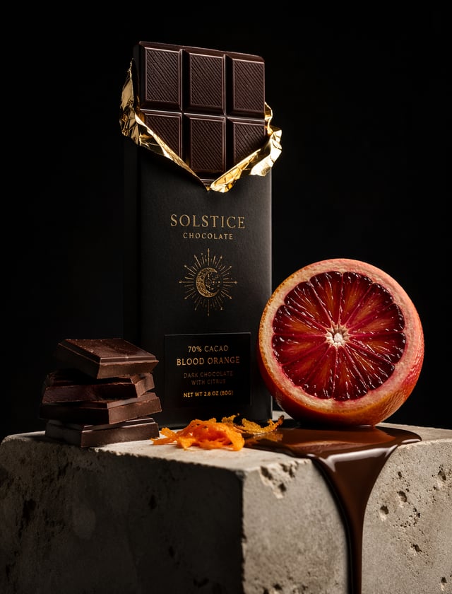 A premium dark chocolate bar wrapped in matte black paper with gold foil accents stands upright on a