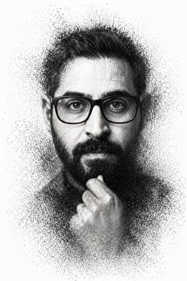 A high-contrast monochrome portrait depicts a man with a groomed beard and thick-rimmed glasses, his