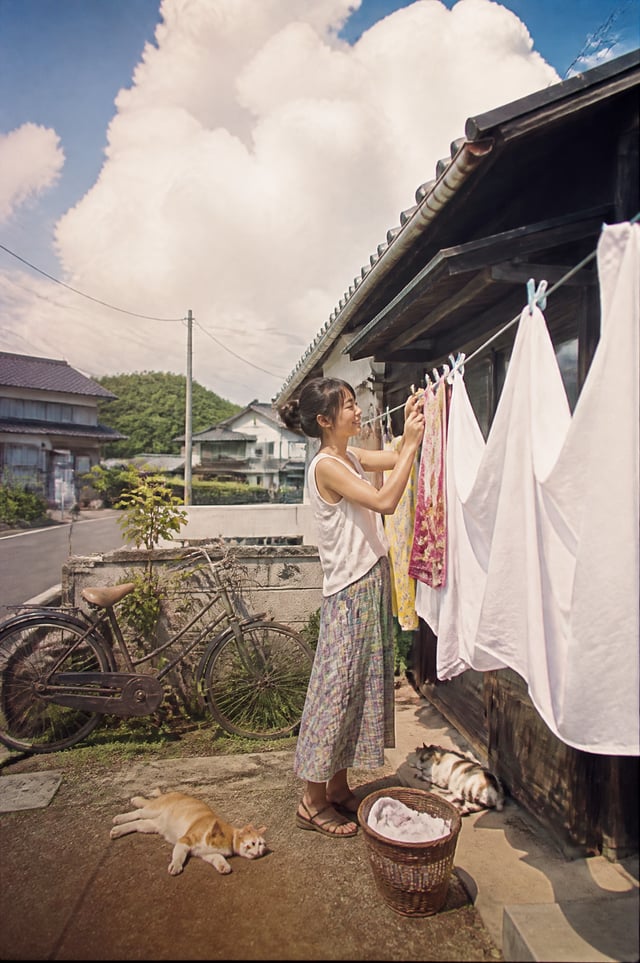 A beautiful Japanese woman hanging freshly washed white linen outside a tiny wooden house on a peace