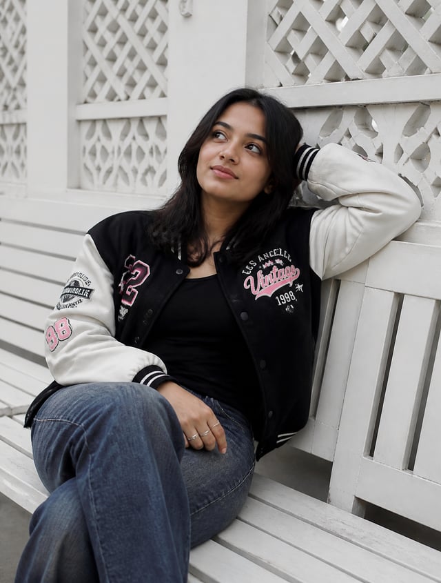 A young woman is sitting casually on a white wooden bench, positioned slightly off-center, with her 