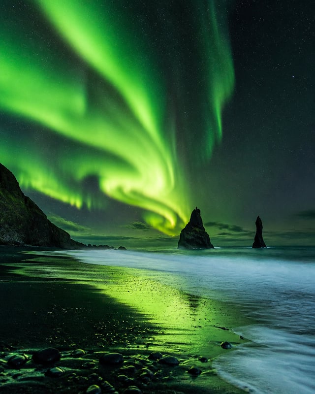 Create a breathtaking realistic travel photograph of a massive glowing green aurora borealis swirlin