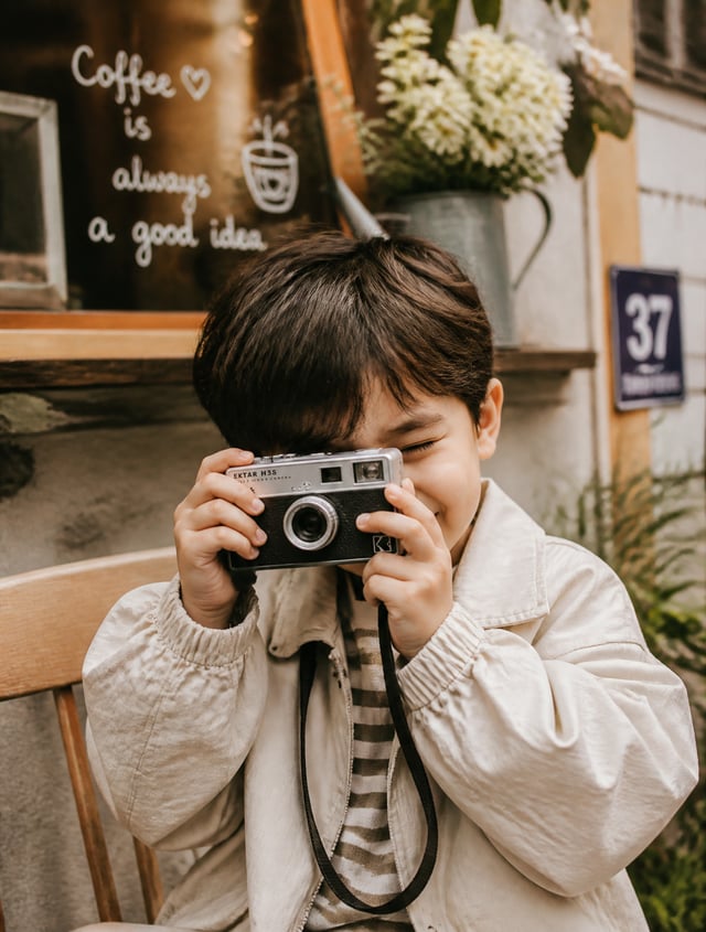 A cute picture of a young boy holding a mini retro camera, actively capturing a candid moment to pre
