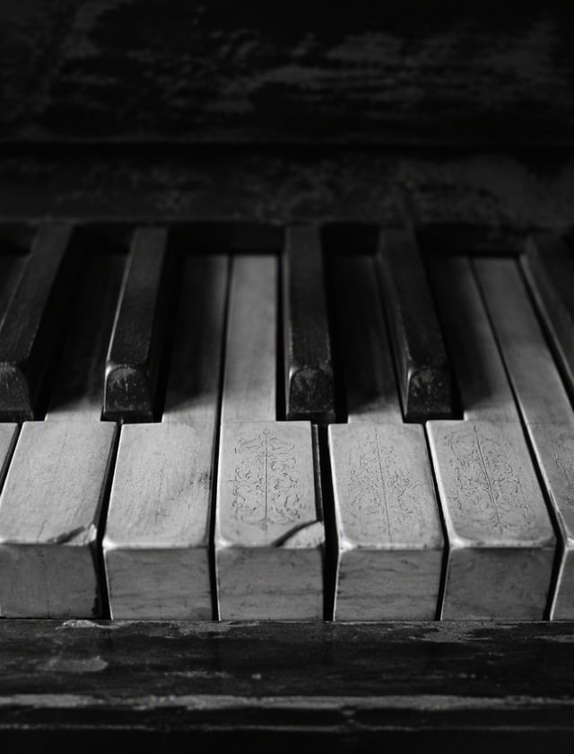 A high-contrast, black and white photo of a close-up of weathered piano keys. The keys have a mosaic