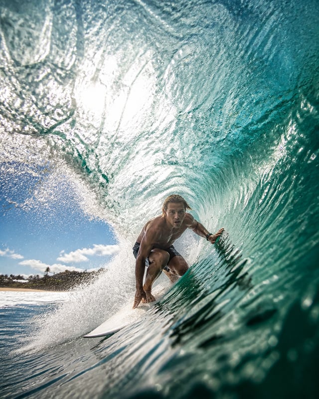 Create a dynamic cinematic sports photograph of a surfer riding inside the curl of a massive translu