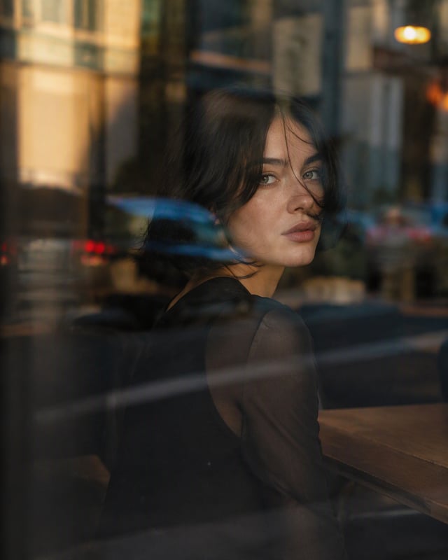 Ultra-cinematic close-up portrait of a young woman sitting inside a dark urban café, photographed fr