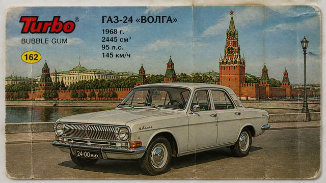 Создай ГАЗ-24 "Волга", 1968 года выпуска, в виде вкладыша от жвачки Турбо. На фоне изобрази Кремлёвс