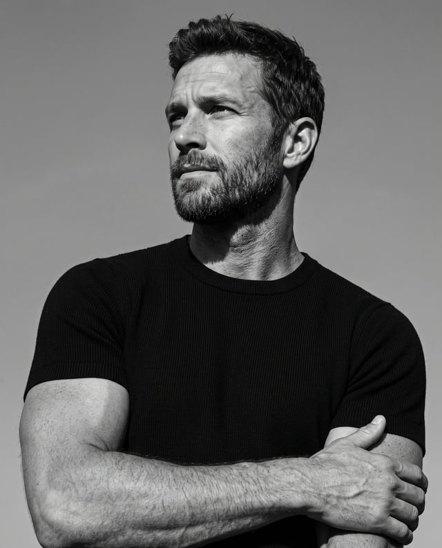 Ultra-realistic black-and-white editorial portrait, low-angle shot, 4:5 aspect ratio. The man fills 