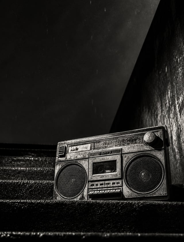 A weathered vintage boombox rests on rain-slicked concrete steps in this dramatic black and white ph