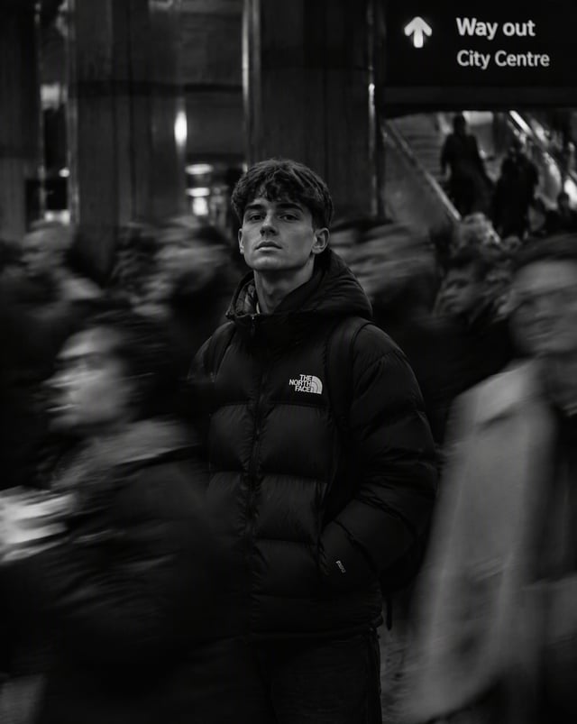 Black-and-white cinematic portrait of a young person in a The North Face puffer jacket standing stil