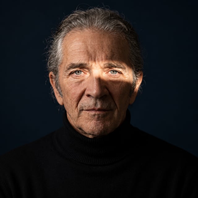 [UPLOAD YOUR IMAGE] An elderly man with swept-back silver hair and weathered facial features faces t