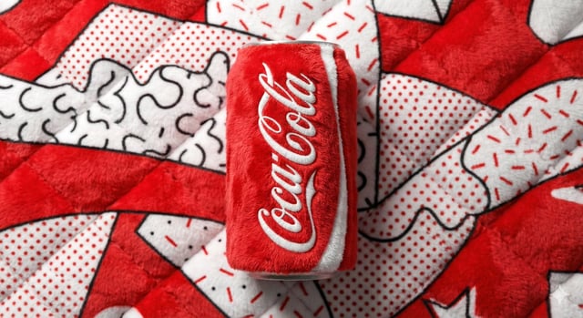 A beverage can branded [BRAND NAME], entirely made from vibrant, fluffy plush fabric, positioned cen