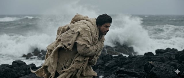 Wide shot, subject acts as an anchor against a raging wind. Standing on a jagged black rock coastlin