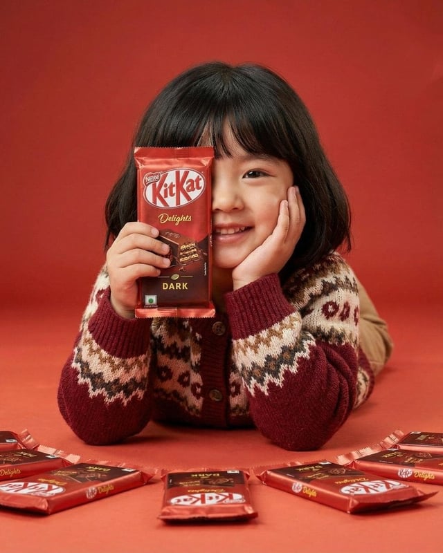 A cute young girl with short black hair and bangs smiling while holding a red KitKat Dark chocolate 