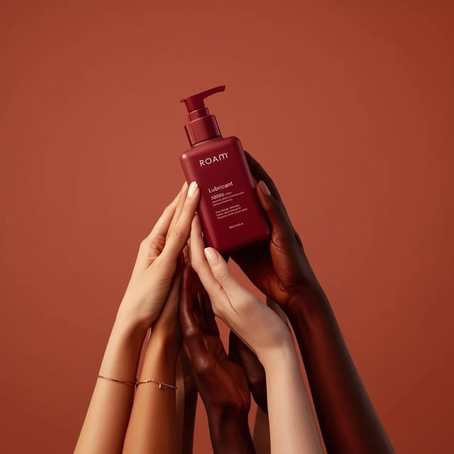 Minimalist product photography of a matte red pump bottle labeled ‘ROAM lubricant’, held by multiple