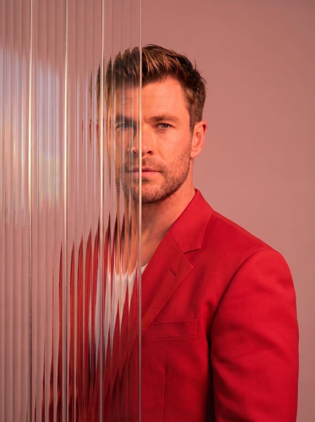 A striking editorial portrait photograph of a person wearing a red blazer, shot against a soft light