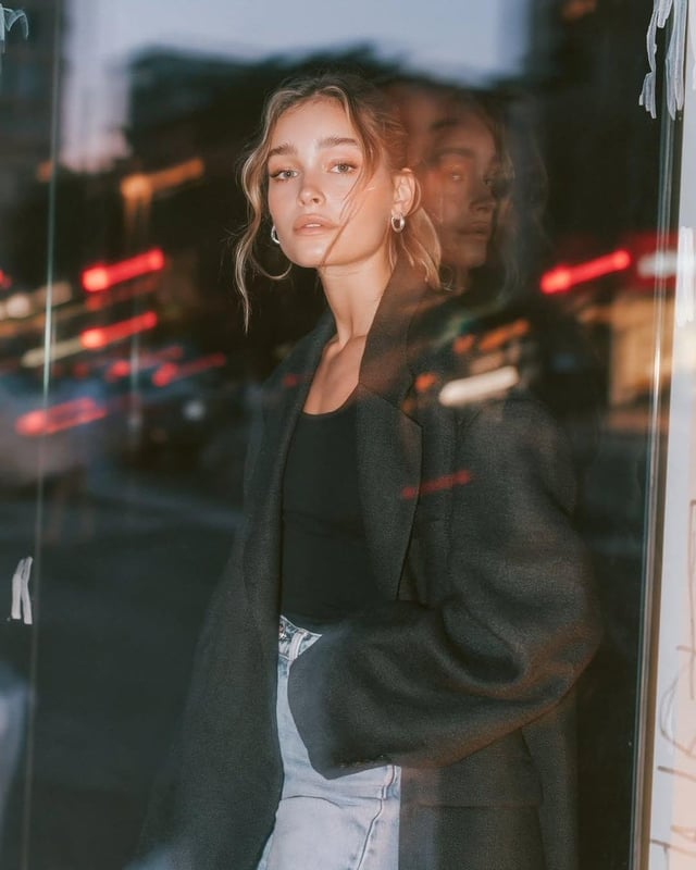 Ultra-realistic editorial fashion portrait of a young woman standing beside a large glass storefront