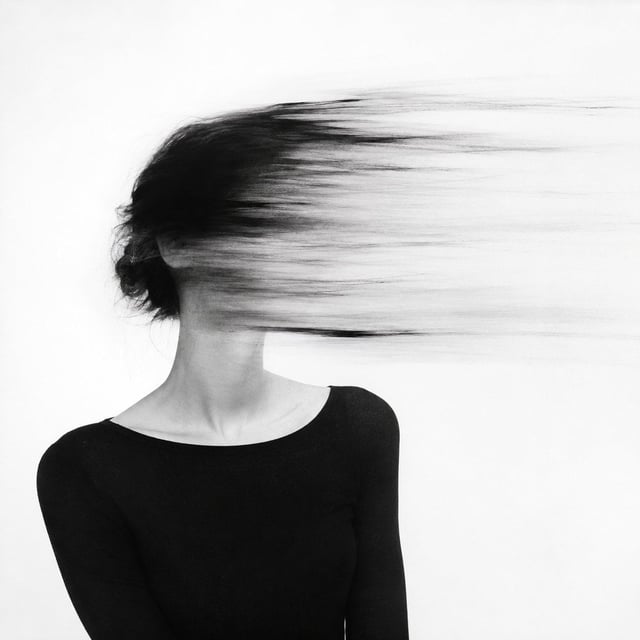 An abstract black and white psychological portrait of a woman whose head and face are slowly being e