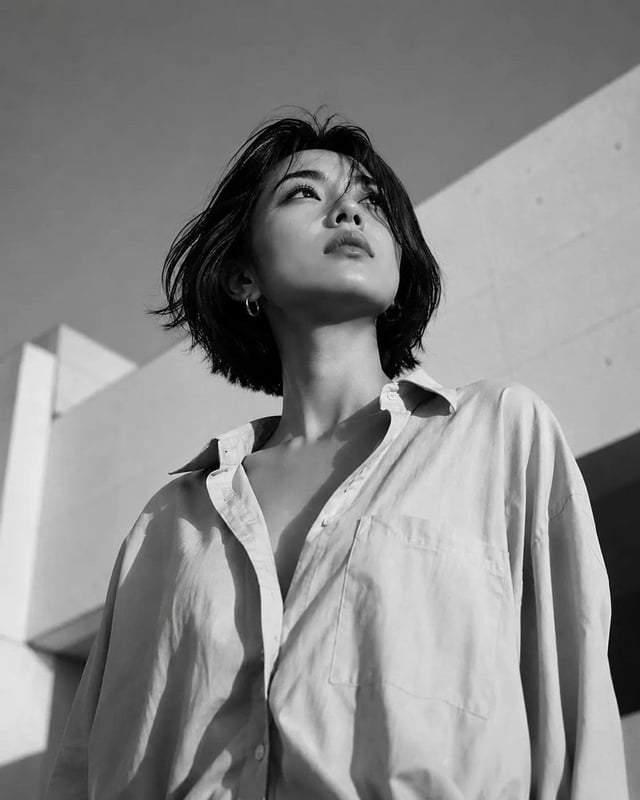 Low-angle fashion editorial shot of an East Asian woman with a short black bob hairstyle, gazing upw