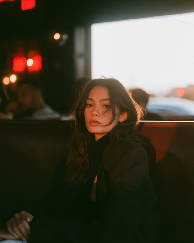 A cinematic café portrait of a beautiful young woman sitting alone in a cozy retro diner at sunset, 