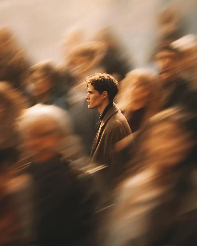 A cinematic street portrait of a solitary young man standing perfectly still in the middle of a fast