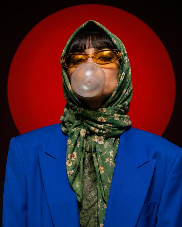 A stylized portrait photograph against a large red circular background. The subject wears a bright b