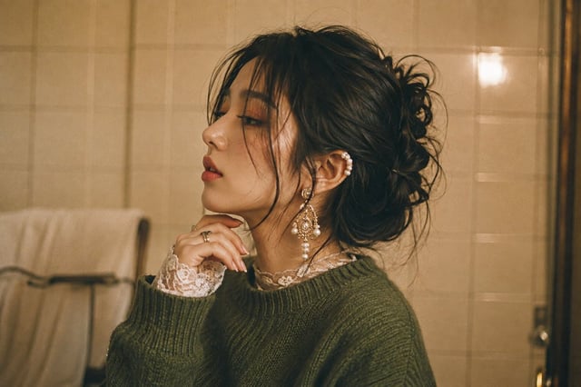 Side-profile medium shot of a young East Asian woman with messy dark hair tied in a loose textured u