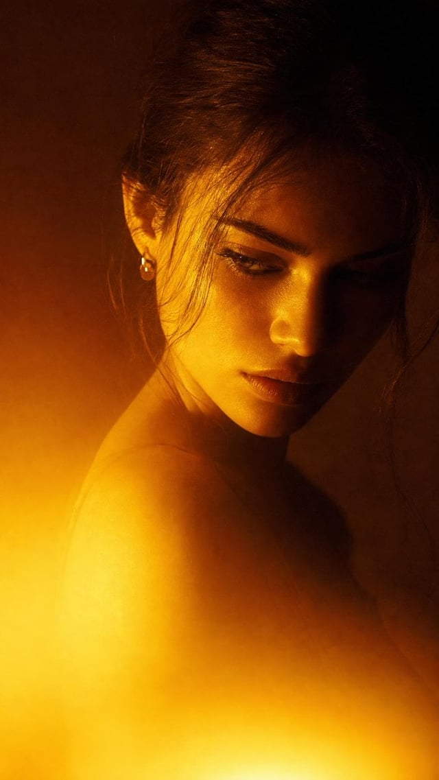 Dramatic close-up portrait with warm colored lighting, a woman with slightly tousled and natural-loo